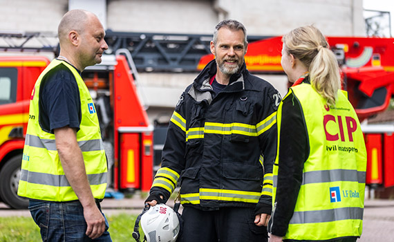 Man från räddningstjänsten med hjälm i handen pratar med två civila insatspersoner